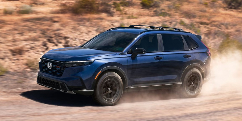 Blue Honda CR-V driving on a dirt road, kicking up dust.