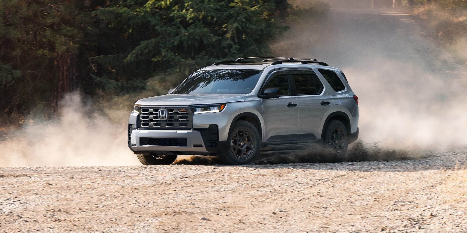 Silver Honda Pilot TrailSport kicking up dust on a dirt road.